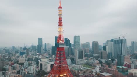 Drohnenantenne-über-Der-Stadt-Tokio,-Die-Während-Eines-Atemberaubenden-Sonnenuntergangs-Mit-Blauem-Und-Orangefarbenem-Himmel-Um-Den-Berühmten-Roten-Tokio-Turm-Herumschwenkt,-Der-Von-Hohen-Wolkenkratzern-Umgeben-Ist
