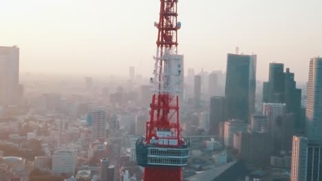 Drohnenantenne-über-Der-Stadt-Tokio,-Die-Während-Eines-Atemberaubenden-Sonnenuntergangs-Mit-Blauem-Und-Orangefarbenem-Himmel-Um-Den-Berühmten-Roten-Tokio-Turm-Herumschwenkt,-Der-Von-Hohen-Wolkenkratzern-Umgeben-Ist