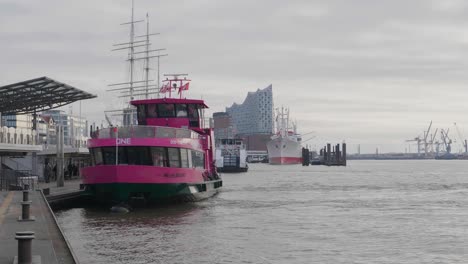 a-pink-ferry-boat-in-Hamburg,-Germany-with-the-famous-Elbphilharmonie-in-the-background