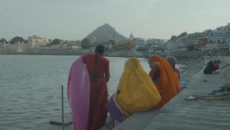 Hinter-Drei-Indischen-Frauen,-Die-Traditionelle-Saris-Tragen,-Sitzen-Sie-Am-Ufer-Des-Wunderschönen-Ganges