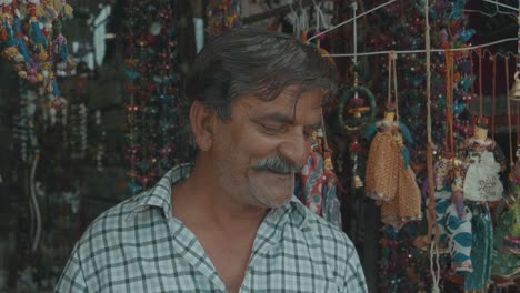 Un-Hombre-Indio-De-Aspecto-Muy-Cálido-Y-Acogedor-Parado-Frente-A-Su-Tienda-Callejera-En-Pushkar,-India