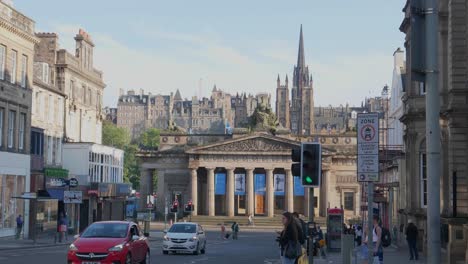 Streets-of-Edinburgh-with-pedestrians,-cars-in-the-foreground-and-castle-hill-in-the-background