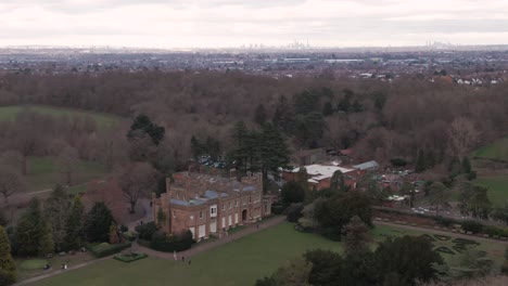Aerial-drone-shot-of-Addington-Palace-in-Croydon,-London,-United-Kingdom-on-a-cloudy-day-and-with-London-Downtown-Cityscape-in-the-background