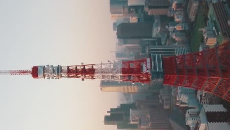 VERTICAL---Drone-aerial-above-Tokyo-City-panning-around-the-iconic-red-Tokyo-Tower-surrounded-by-tall-skyscrapers-during-a-stunning-sunset-with-blue-and-orange-skies