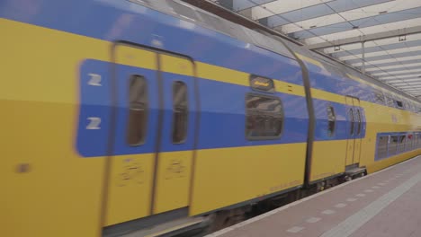Un-Enorme-Tren-Regional-Azul-Y-Amarillo-Que-Sale-De-La-Estación-Principal-De-Trenes-De-Rotterdam,-Países-Bajos