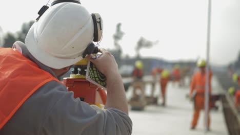 Surveyor-takes-measurements-using-laser-rangefinder-at-construction-site,-rear-view