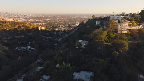 Zur-Goldenen-Stunde-Fliegen-Wir-über-Die-Hügel-Hollywoods,-Luxusanwesen-Eingebettet-In-Bewaldete-Hügel-Mit-Goldenem-Sonnenuntergang-Am-Horizont