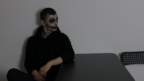 A-man-with-dark-clown-makeup-sitting-alone-and-looking-towards-the-wall-while-listening-and-being-thoughtful