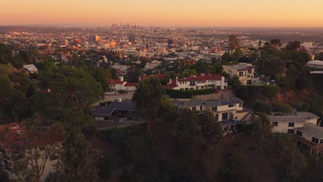 Drohnenaufnahmen-über-Häusern-In-Den-Hollywood-Hills-Mit-Der-Skyline-Von-Los-Angeles-Im-Hintergrund-Bei-Sonnenuntergang
