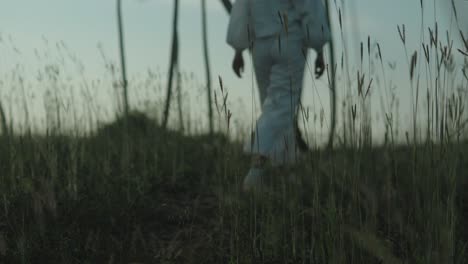 Person-walking-through-tall-grass-field-at-dusk,-low-angle-view