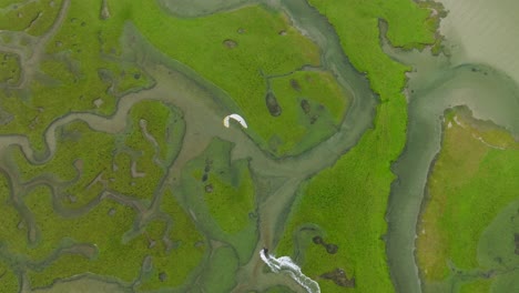 Wide-aerial-birdseye-view-of-a-kitesurfing-adventurer-sailing-through-a-bright-green-river-delta-on-the-island-of-Achill-in-Ireland