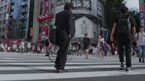 Many-japanese-people-cross-a-packed-road-in-Shinjuku,-Tokyo-while-rush-hour-with-the-famous-Don-Quijote-Building-appearing-at-the-end