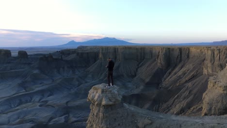 Ein-Einzelner-Drohnenbetreiber-Steht-Auf-Einer-Wüstensteinsäule-Und-Fliegt-Eine-Drohne-Während-Des-Sonnenuntergangs-Am-Moonscape-Overlook-In-Utah