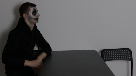 Young-Caucasian-man-with-dark-clown-Halloween-makeup-sitting-alone-and-looking-at-the-wall