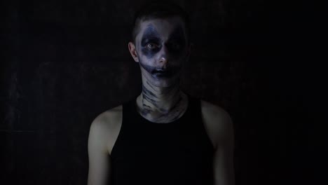 Young-Caucasian-man-with-a-scary-dark-Halloween-clown-makeup-costume-standing-in-front-of-a-black-background