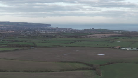 Establishing-Aerial-Shot-of-Fields-with-Whitby-in-the-Distance-Coastline