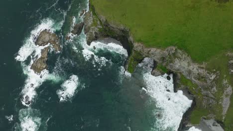 Luftaufnahme-Von-Wellen,-Die-Auf-Einer-Küstenklippe-Mit-Hellgrünem-Gras-Auf-Der-Insel-Achill-In-Irland-Krachen