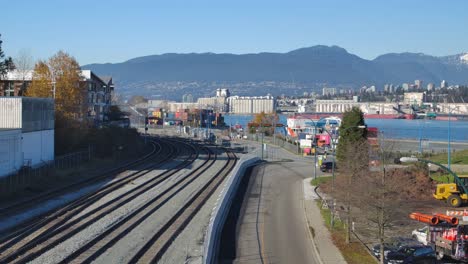 Railway-tracks-leading-into-an-industrial-port-in-Vancouver,-clear-blue-sky,-mountains-in-the-background,-daytime