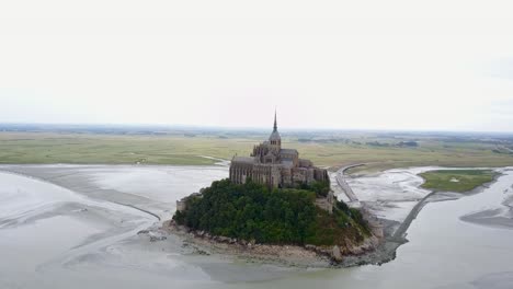 Flying-behind-the-Mont-Saint-Michel-in-France,-when-the-water-tide-is-down