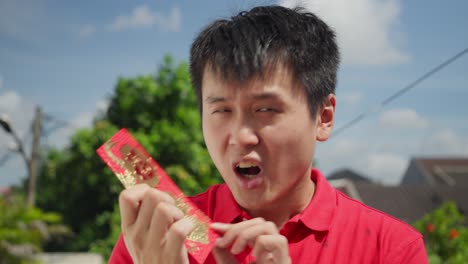 Ein-Chinesischer-Mann-Hält-Aufgeregt-Das-Leuchtend-Rote-Hong-Bao-In-Der-Hand,-Das-Das-Chinesische-Neujahr-Symbolisiert