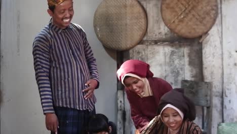 Happy-Javanese-family-with-their-two-children-in-front-of-an-ancient-kitchen,-Central-Java,-Indonesia_tilt-up-shot
