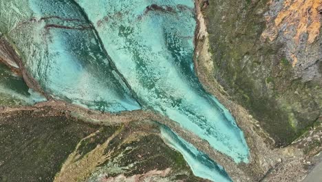 Aerial-drone-with-a-rotating-and-ascending-right-slow-movement,-capturing-the-base-of-Grænihryggur-and-the-glacial-river,-the-green-rock-in-Landmannalaugar,-Iceland,-medium-tones-of-orange-and-green