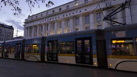 The-Palace-of-Justice-in-the-evening,-a-modern-tram-and-people-passing-by