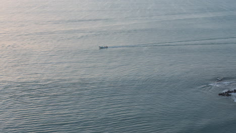 Small-boat-cruising-on-calm-waters-near-Coronado-at-dusk,-creating-ripples,-aerial-view