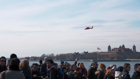 US-Coast-Guard-helicopter-flying-over-Ellis-Island-with-people-on-a-ferry-in-the-foreground-at-slow-motion