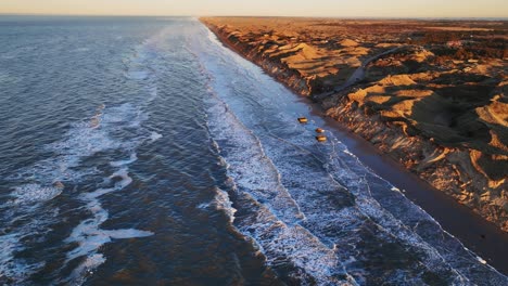 Aerial-view-North-Sea-water-washes-the-beach-with-high-dunes-on-a-cold-winter's-evening-when-the-sun-is-setting