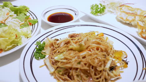 Panning-from-the-left-to-the-right-on-a-meal-served-in-a-restaurant,-a-plate-of-salad,-stir-fried-noodles,-and-fried-dumplings