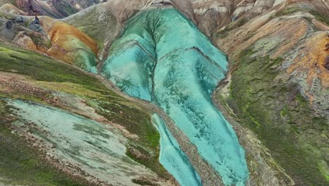 Aerial-drone-with-a-fast-backward-movement-and-a-slow-sliding-down-over-Grænihryggur,-the-green-rock,-in-Landmannalaugar,-Iceland,-emphasizing-the-medium-tones-of-orange-and-green