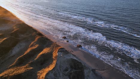 Bird-eye-view-North-Sea-water-washes-the-beach-with-high-dunes-on-a-cold-winter's-evening-when-the-sun-is-setting