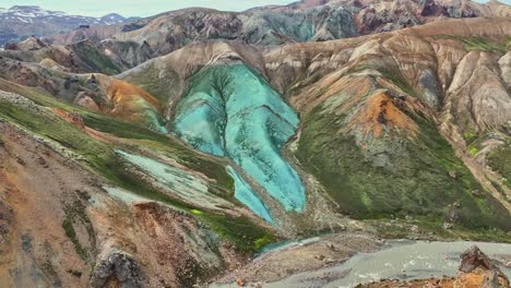 Aerial-drone-fast-backward-movement-at-medium-altitude,-over-Grænihryggur,-the-green-rock,-the-river,-and-the-valley-in-Landmannalaugar,-Iceland,-highlighting-medium-tones-of-orange-and-green