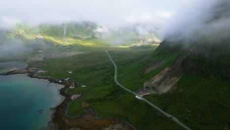 An-aerial-view-reveals-cars-driving-through-while-low-hanging-clouds-are-above,-in-the-captivating-landscape-of-the-Lofoten-Islands,-Norway