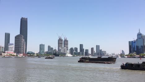 Barcos-Que-Transportan-Diversos-Bienes-Y-Materiales-En-El-Río-Huangpu-En-Pudong,-Shanghai,-Rascacielos-En-Segundo-Plano.