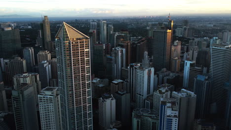 Drone-circling-sunlit-high-rise-of-Makati-city,-evening-in-Manila,-Philippines