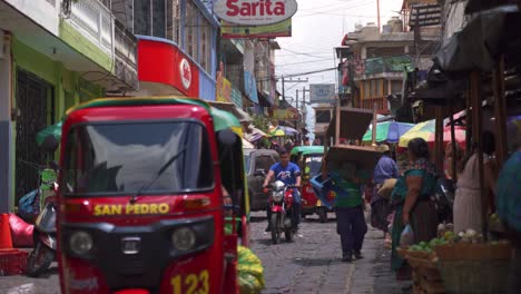 Busy,-colourful,-crowded-street-with-people,-cars,-bikes,-tuk-tuks-and-a-dog-in-San-Pedro,-Lake-Atitlan,-Guatemala