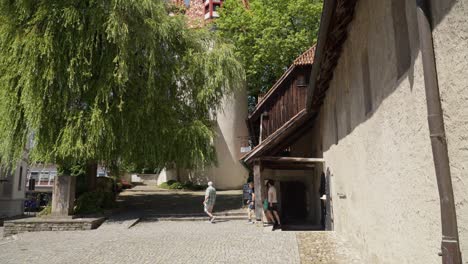 Willow-trees-and-visitors-near-medieval-towers-in-Lindau,-Bodensee,-on-a-sunny-day