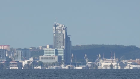 Skyline-of-Gdynia,-Poland,-viewed-across-water,-featuring-Sea-Towers,-a-prominent-skyscraper,-with-cranes-of-the-shipyard,-other-modern-buildings,-and-a-clear-sky-reflecting-the-city's-maritime