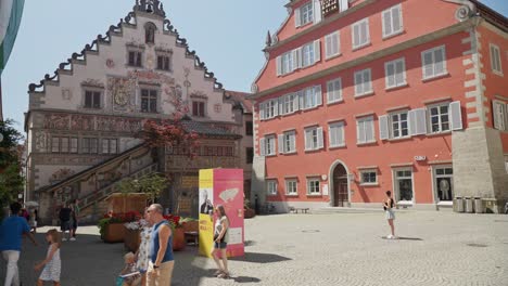 Sunny-day-in-Lindau-with-tourists-strolling-by-historic-painted-buildings,-clear-blue-sky