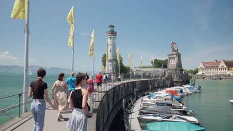 Sunny-day-at-Lindau-Harbor-with-tourists,-lighthouse,-and-boats-on-Lake-Constance,-clear-sky