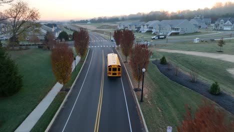 American-school-bus-driving-through-new-housing-development-at-sunrise-in-autumn