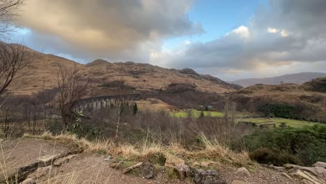 Hikers-overlooking-the-historic-Glenfinnan-Viaduct-amidst-Scottish-Highlands,-cloudy-skies,-timelapse