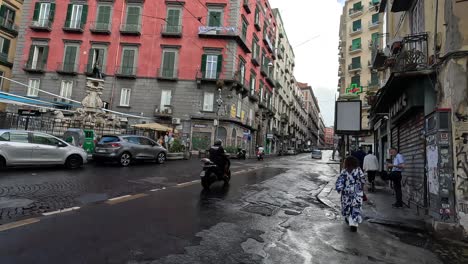 Rainy-street-with-car,-scooter-and-walking-tourists-in-Naples-city-center-in-Italy