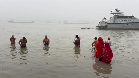 Static-view-of-men-and-woman-bathing-and-praying-in-a-winter-morning-during-Sankranti-festival-with-jetty-in-the-background-in-Babughat,-Kolkata