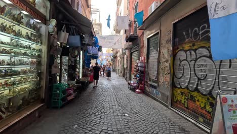 POV-shot-of-walking-a-narrow-street-with-graphite-in-the-city-centre-with-shops-with-souvenirs-of-Naples-in-Italy