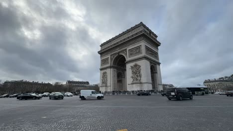 Wide-angle-shot-of-the-Arc-de-Triomphe-in-Paris-with-bustling-traffic,-cloudy-sky,-timelapse