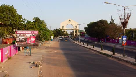 Static-aerial-view-of-the-arch-and-city-of-Banjul,-Gambia-taken-by-the-highway-side-with-cars-passing