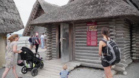 Visitors-at-an-Ice-Age-museum-in-Friedrichshafen-with-a-thatched-roof-structure,-lake-view